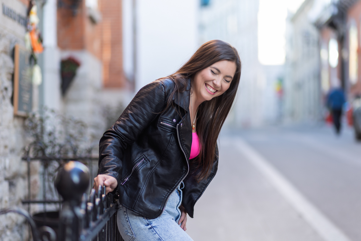 Femme en veste de cuir souriant dans une rue pavée