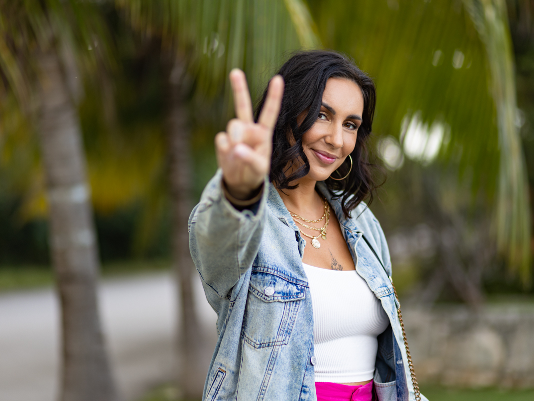 Femme en veste de jean faisant le signe de la paix devant des palmiers