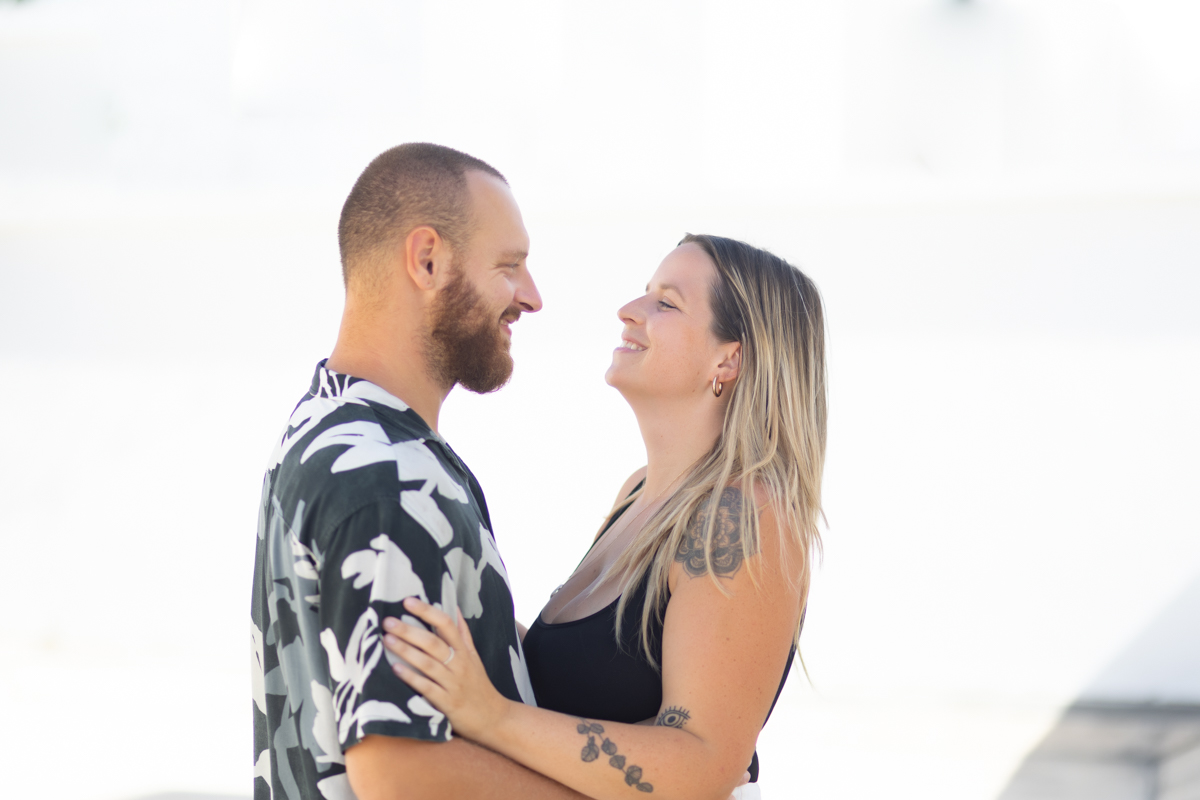 A happy couple embraces each other in front of a pristine white wall in Playa del Carmen, their smiles radiating joy and love against the vibrant backdrop.