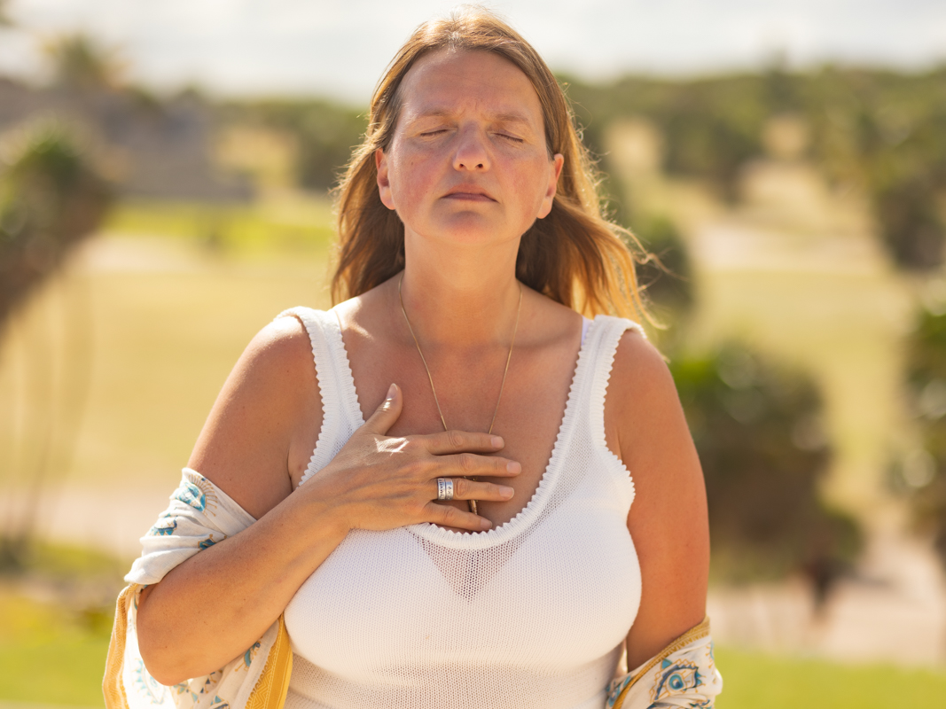 Femme la main sur le coeur, les yeux fermés, dans un champ ensoleillé