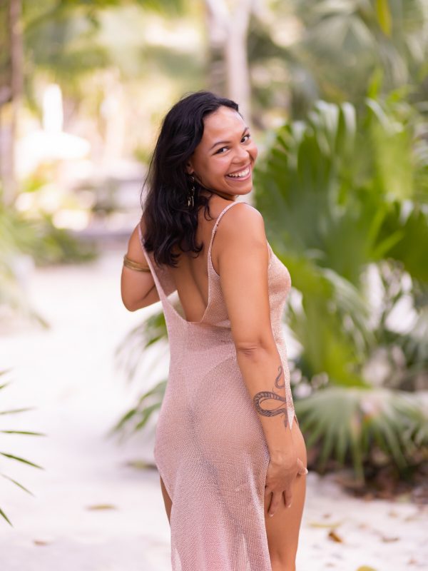 A woman with a radiant smile poses for the camera in a mesmerizing Tulum cenote, surrounded by crystal-clear turquoise water and lush greenery.