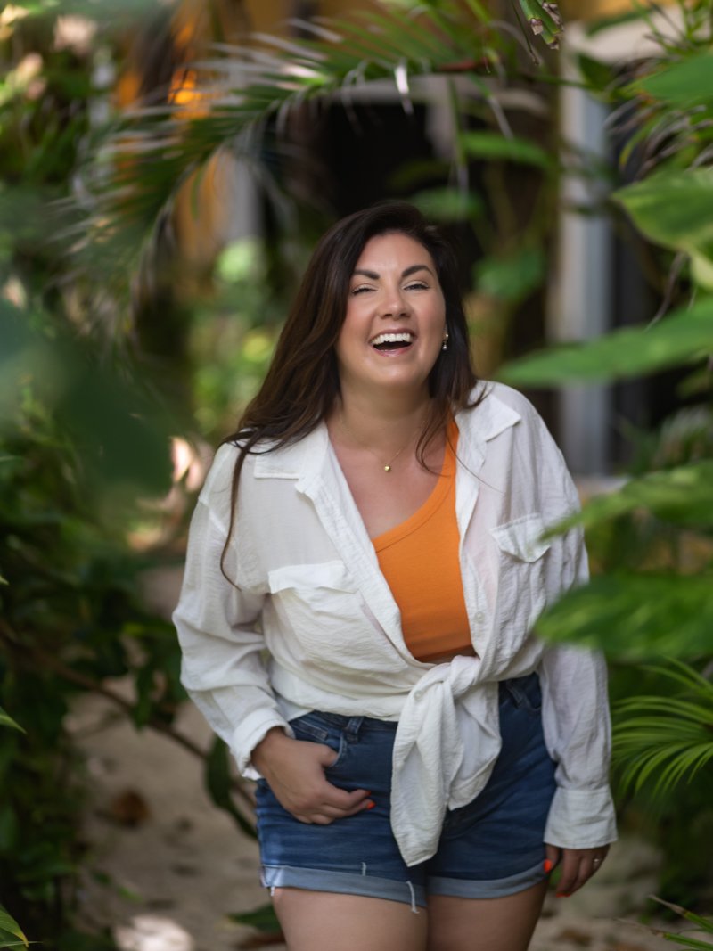 Femme en chemise blanche riant devant un feuillage tropical